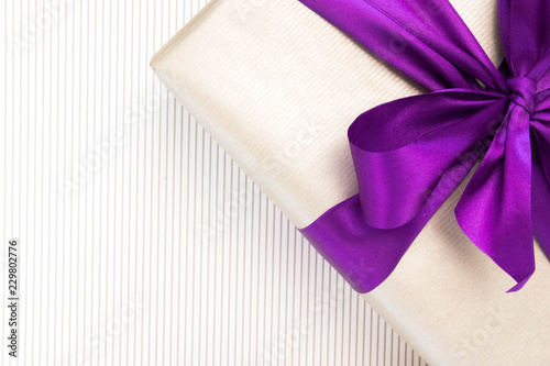Gift with violet ribbon and bow-knot on light background. Copy space.