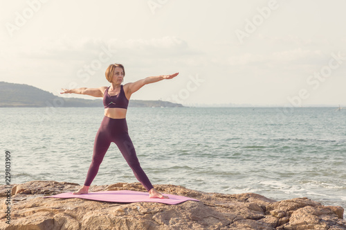 Mature woman doing yoga on the beach at sunset.