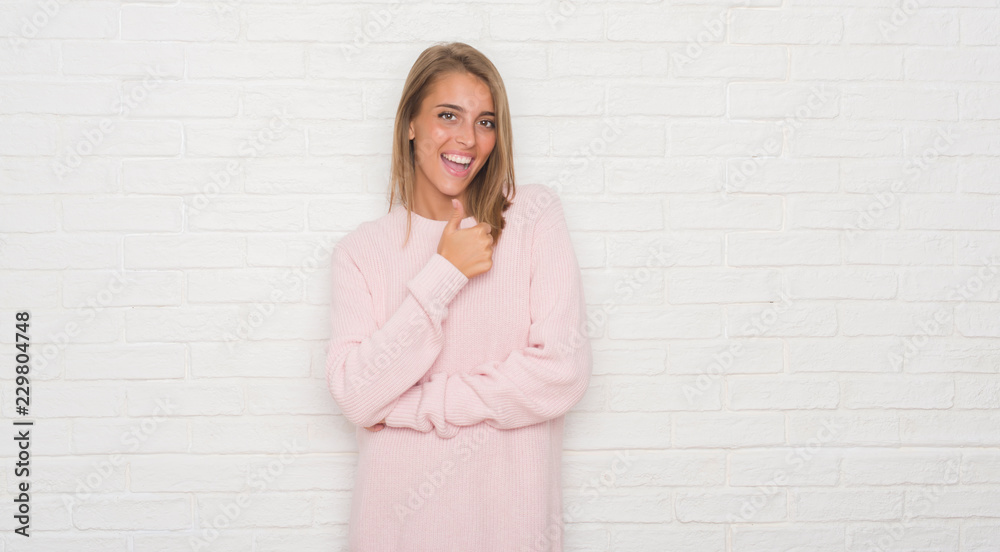 Beautiful young woman over white brick wall happy with big smile doing ok sign, thumb up with fingers, excellent sign Beautiful young woman over white brick wall happy with big smile doing ok sign, thumb up with fingers, excellent sign