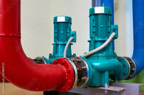 Two vertical engines painted blue with pumps connected to pipes painted red and blue.