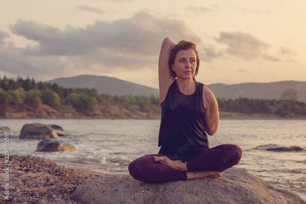 Fototapeta premium Woman practicing yoga on the beach at sunset.