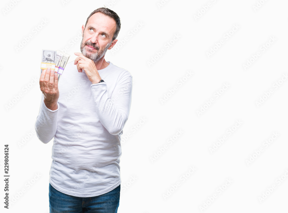 Senior hoary man holding buch of dollars over isolated background serious face thinking about question, very confused idea Senior hoary man holding buch of dollars over isolated background serious face thinking about question, very confused idea