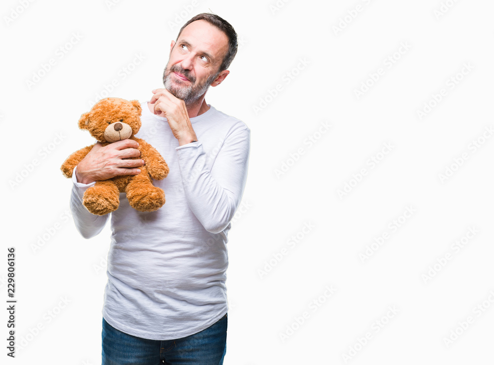 Middle age senior hoary man holding teddy bear over isolated background serious face thinking about question, very confused idea