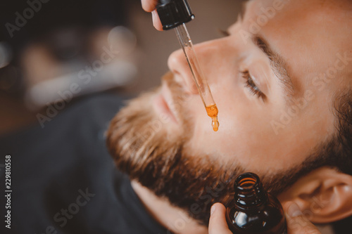 Foto Means for caring beard oil, barber puts on face of man.