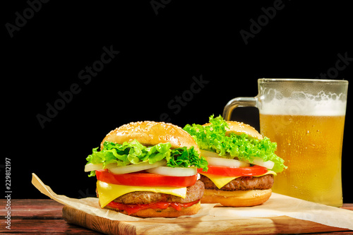 Hamburger, fast food, burger, hamburger steak with cutlet, cheese, tomato, onion, lettuce and a glass of beer on a wooden board.