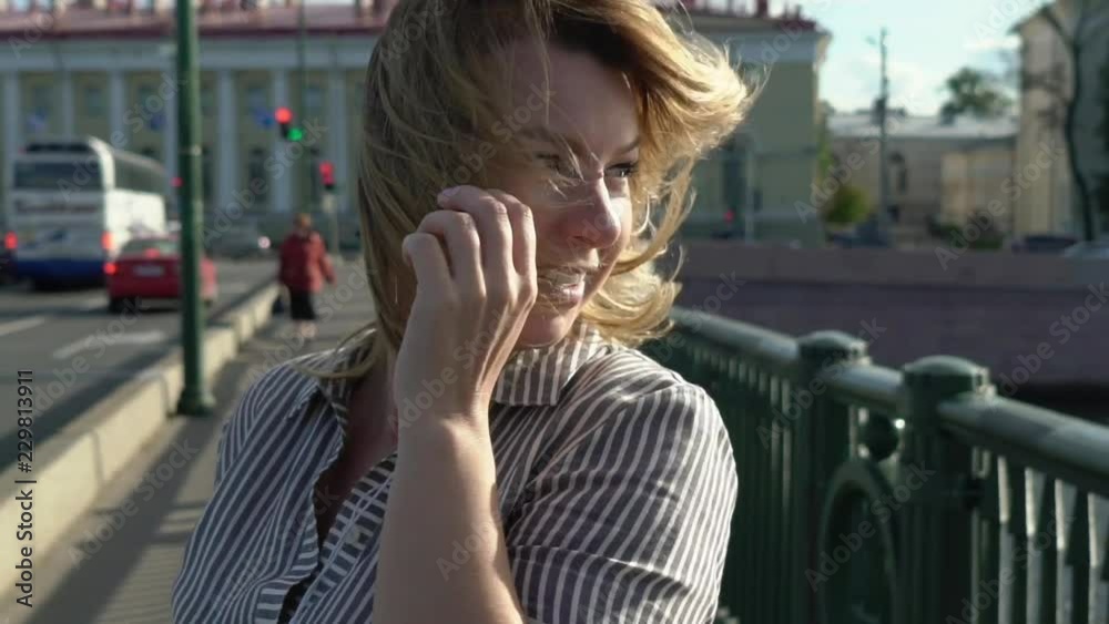 Young blonde woman smiling and posing in a city slowmotion at the summer evening at the bridge Young blonde woman smiling and posing in a city slowmotion at the summer evening at the bridge