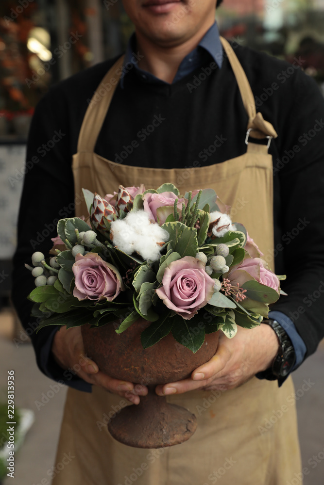 Obraz premium Festive flower arrangement of paleviolet roses and cotton flowers in the vase florist holding at the flowers boutique.