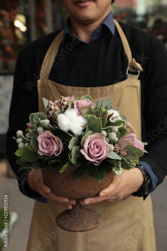 Festive flower arrangement of paleviolet roses and cotton flowers in the vase florist holding at the flowers boutique. photo