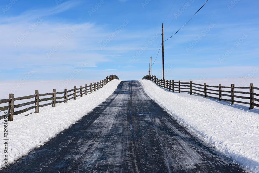 Rural Road with Fence after Winter Snow - looking up small hill and blue skies Rural Road with Fence after Winter Snow - looking up small hill and blue skies
