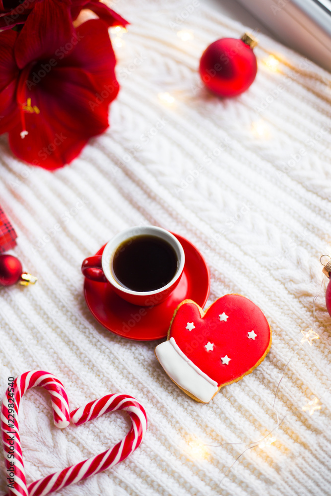 Red cup with espresso coffee and gingerbread in form of glove on white knitted plaid surrounded with winter decor.