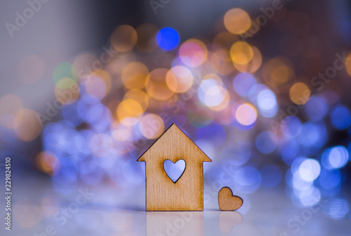 Wooden icon of house with hole in the form of heart with little heart on colorful bokeh background.