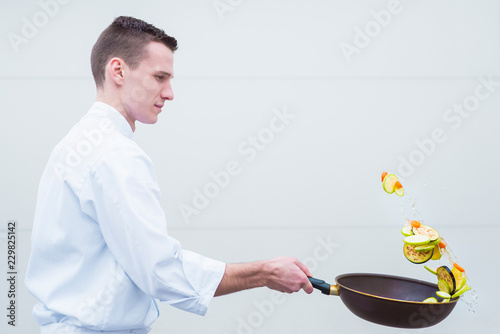 Young chef flipping vegetables in frying pan side view photo