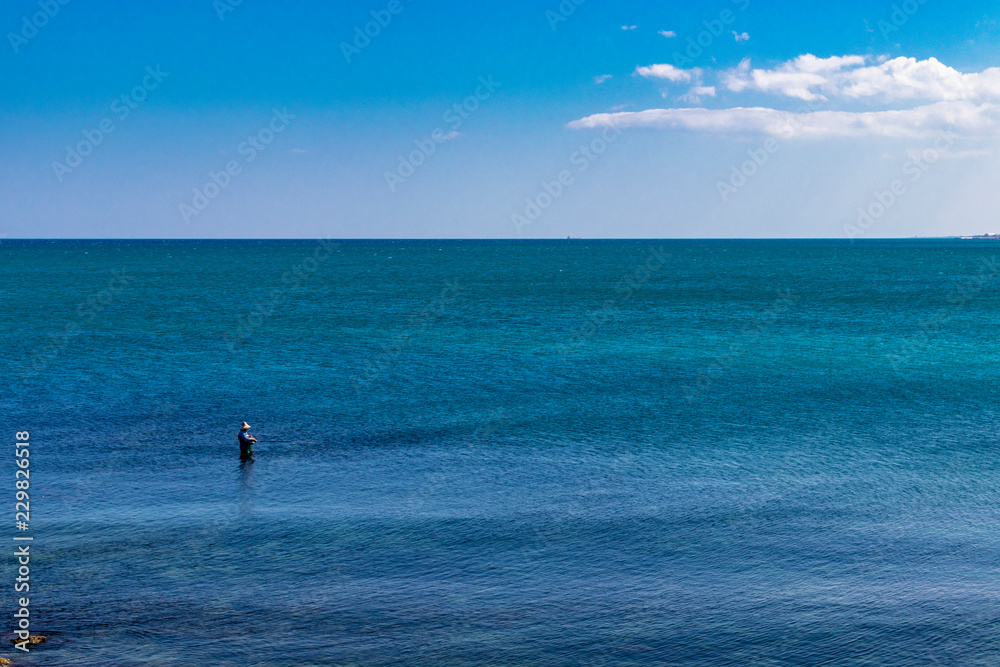 a fisherman fishing in the sea, in the city of Trani, with the Monastery of Santa Maria di Colonna in the background. In Puglia, near Bari, in the province of Barletta, Andria, Trani. Sea and blue sky