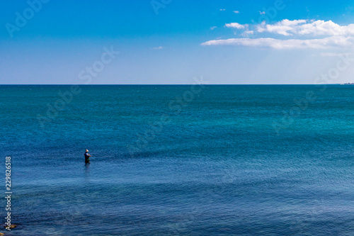 a fisherman fishing in the sea, in the city of Trani, with the Monastery of Santa Maria di Colonna in the background. In Puglia, near Bari, in the province of Barletta, Andria, Trani. Sea and blue sky photo