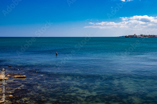 a fisherman fishing in the sea, in the city of Trani, with the Monastery of Santa Maria di Colonna in the background. In Puglia, near Bari, in the province of Barletta, Andria, Trani. Sea and blue sky photo