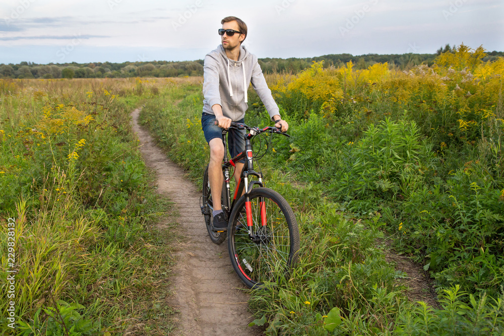 Fototapeta premium Young men on bike in field with flowers, beautiful landscape