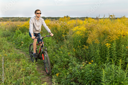 Young man on bike, cyclist in field with flowers, copy space