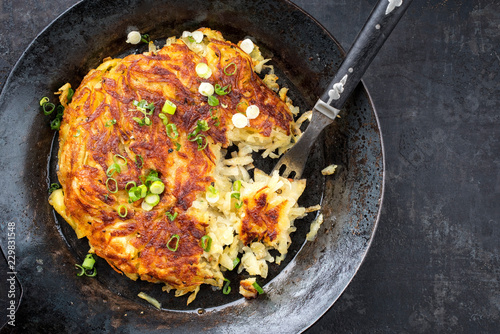 Traditional Swiss rosti as side dish with leek as top view in a frying pan with copy space right photo