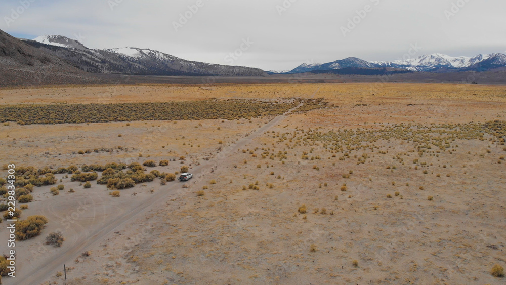 AERIAL: Tourists in an SUV driving down empty gravel road with a view of Rockies