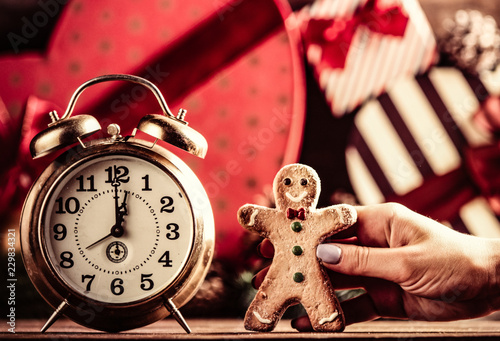 photo of the female hand holding a gingerbread man, alarm clock on the christmas decorations background