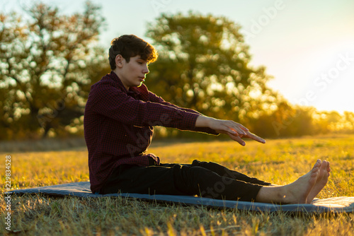 young man doing stretching exercises on the summer field f