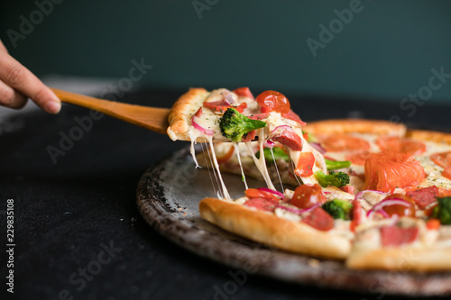 Delicious cheese stringy slice lifted of full supreme pizza baked fresh out of the oven next to ingredients