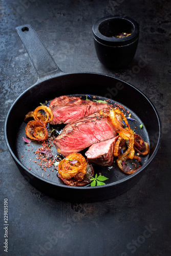 Modern Style classic dry aged sliced roast beef with fried onion rings served as closeup in a minimalistic design cast-iron skillet