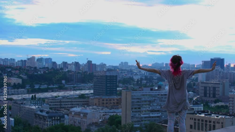 Young female looks at city scape in twilight, pink hair teenager on roof top Young female looks at city scape in twilight, pink hair teenager on roof top