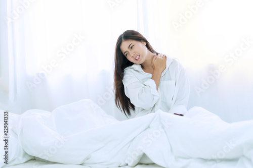 Healthy physical concept. Attractive young woman wake up in the morning on white bed with spine shoulder painful. She hands caught with her neck suffering. Have copy space.