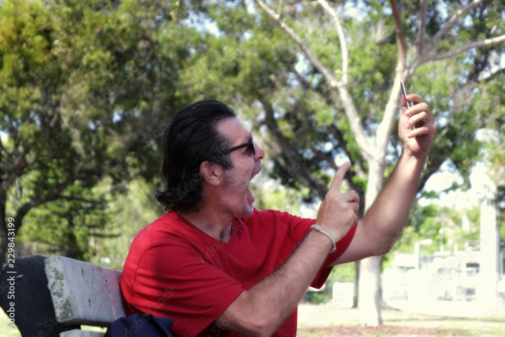 Outdoor portrait of a mid adult man sitting on park bench screeming to mobil phone in Florida, USA Outdoor portrait of a mid adult man sitting on park bench screeming to mobil phone in Florida, USA