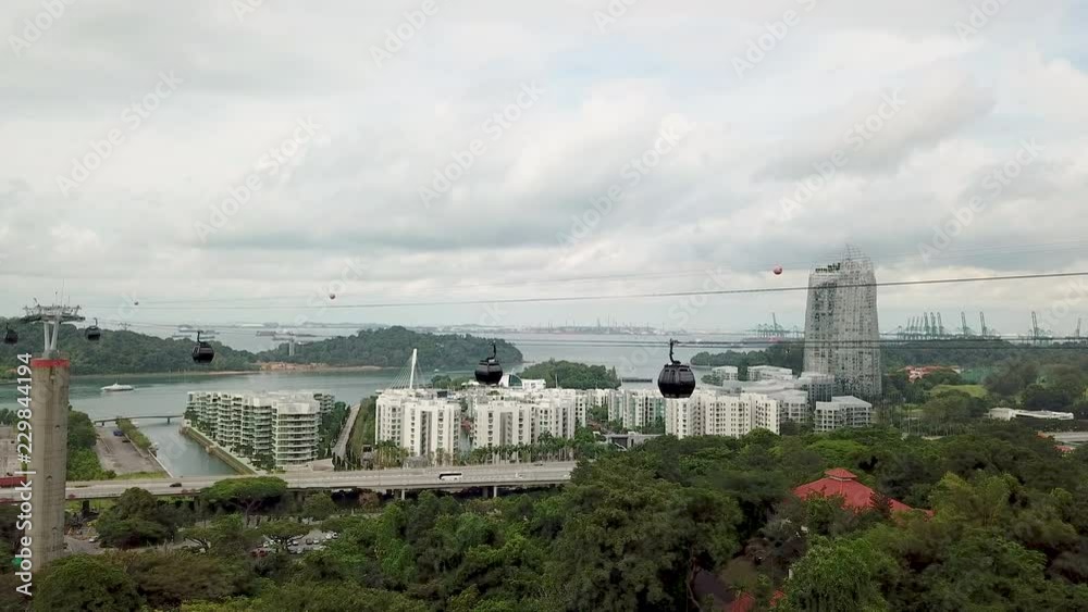 High view above the trees watching the cable cars in Singapore moving across the horizon with passengers High view above the trees watching the cable cars in Singapore moving across the horizon with passengers