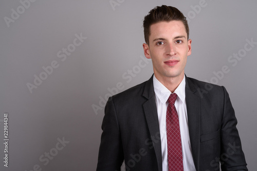 Young handsome businessman wearing suit against gray background
