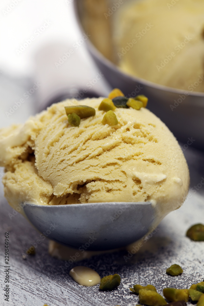 Pistachio ice cream scoop with chopped nuts and white chocolate on a rustic background.