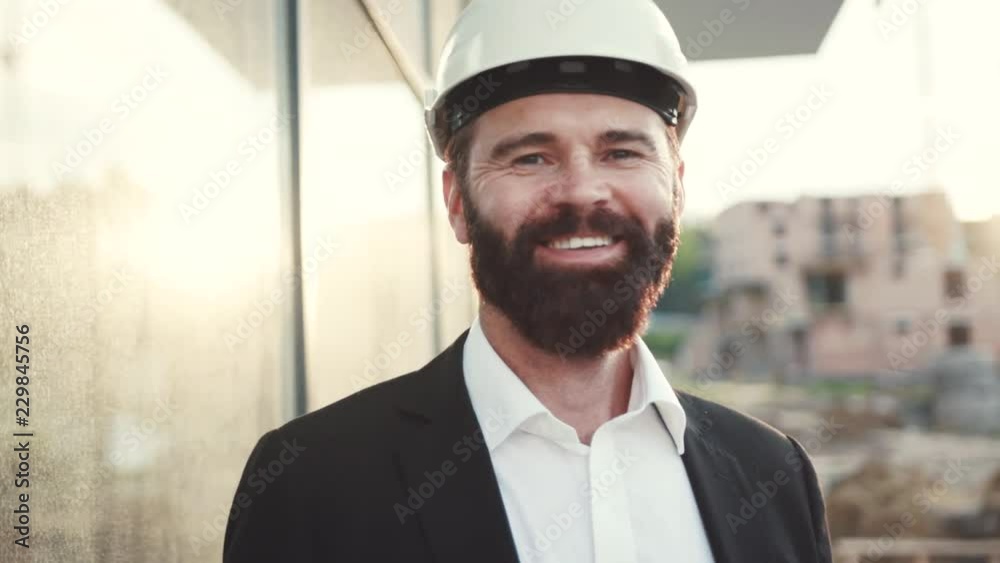 Close up view of handsome joyous bearded caucasian engineer in white safety helmet smiling happily straight to camera. Positive emotions, being happy. Male portrait Close up view of handsome joyous bearded caucasian engineer in white safety helmet smiling happily straight to camera. Positive emotions, being happy. Male portrait