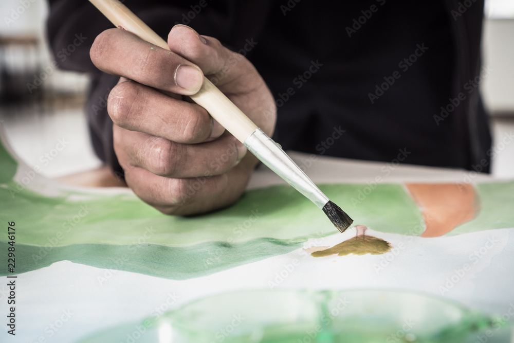 Obraz premium Hands asian student artist painting watercolor abstract of landscape with brush drawing on paper for creation art subject classroom at secondary education in Thailand. Creative skill, Hobbies concept