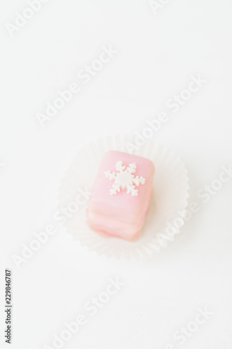 Light pink petit fours, small cake square, covered with sugar icing and decorated with white fondant snowflake © Corinna Haselmayer
