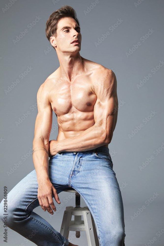 A handsome muscular, shredded man without a shirt, sitting on a chair in  the studio wears only blue jeans. His fitness oiled body is shining. Stock  Photo | Adobe Stock