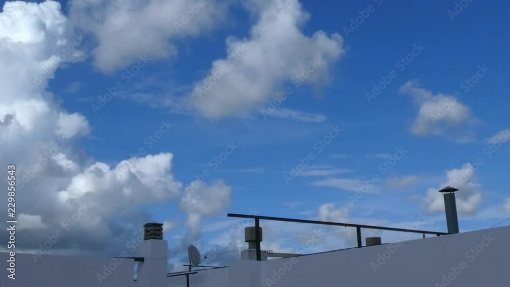 The roof of a building and white clouds passing in a blue sky The roof of a building and white clouds passing in a blue sky