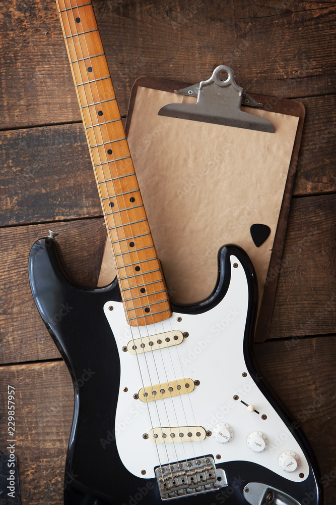 Fototapeta premium Vintage black double cutaway guitar on old wood surface and old clipboard, good for play lists, and production notes. one piece maple neck.