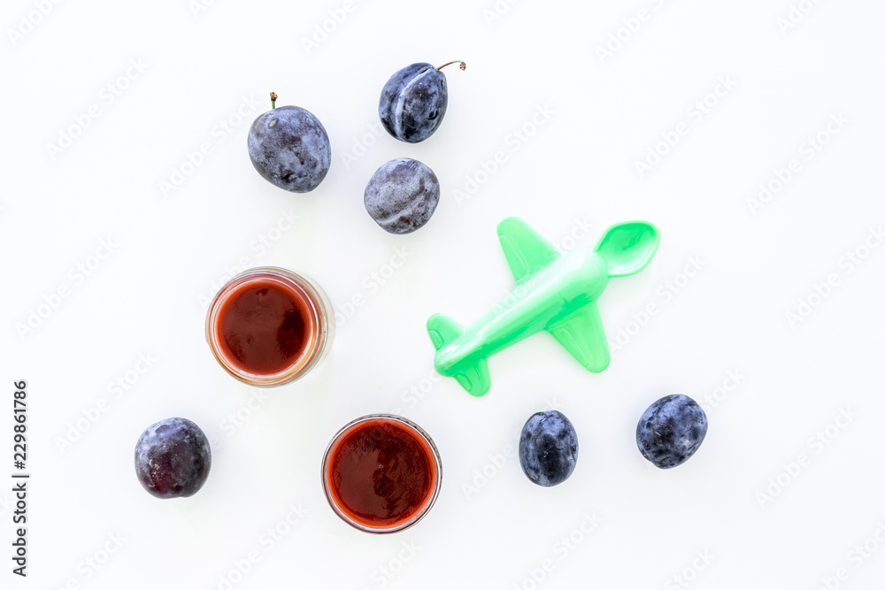 Fruit puree for small babies. Puree with prunes in bowl near punes, spoon, toy on white background top view copy space