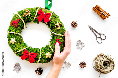 Make traditional green christmas wreath. Female hand hold wreath near matherial for decorative element on white background top view photo