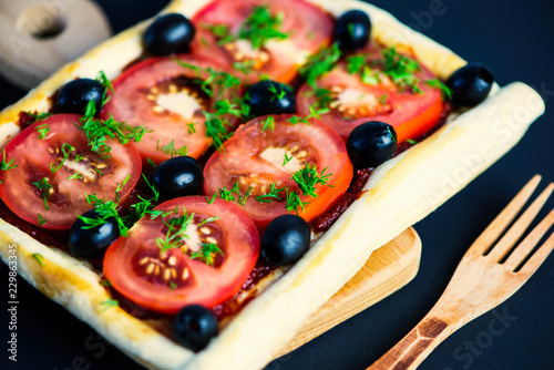 puff pastry cake with tomatoes and olives on a wooden board