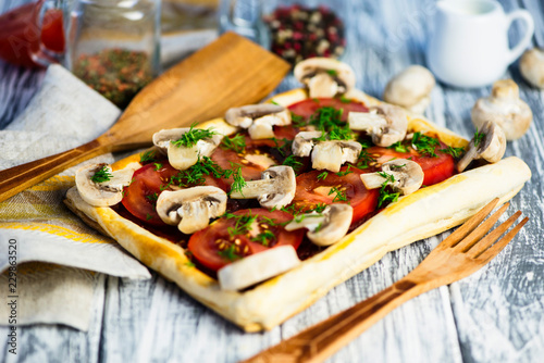 puff pastry pie with tomatoes and mushrooms on a wooden board