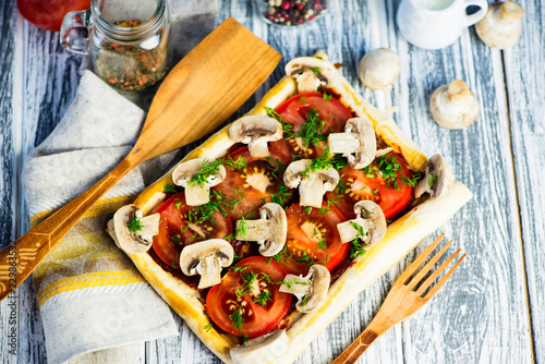 puff pastry pie with tomatoes and mushrooms on a wooden board