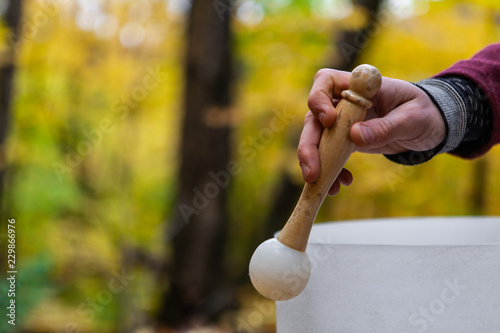 Young Man playing crystal bowls outdoors in the forest while autumn colors are at their best - hand and drumstick, wider angle - With a blurry background in the fall season