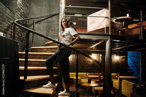 Stylish african american woman in printed t-shirt posed indoor steel stairs.