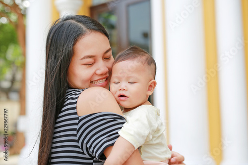 Happy Asian mother carrying her infant outdoor.