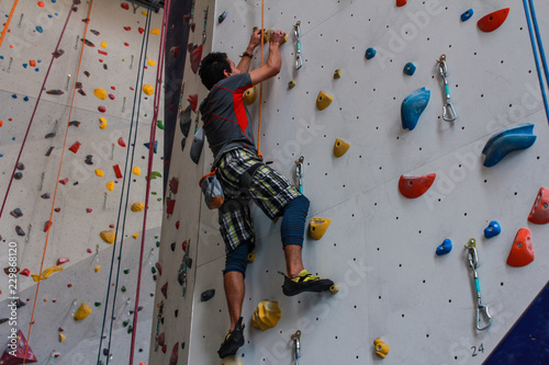 Young man wearing colorful sport clothing climbing on an advanced climbing wall indoors - viewed from the side - Pictures taken in a climbing center in Quebec, Canada.