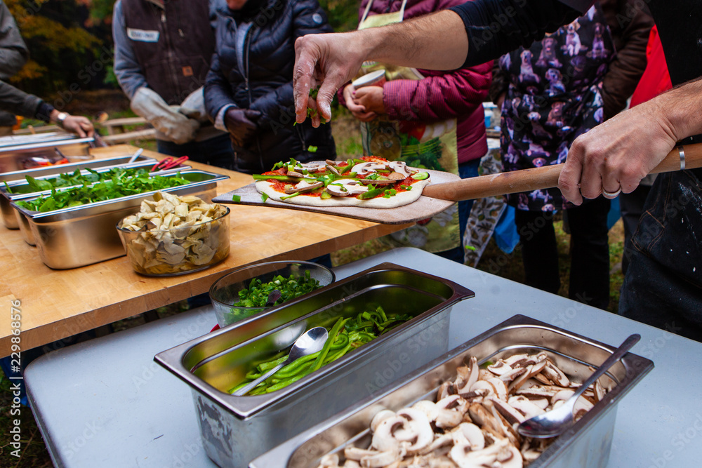 Obraz premium People adding dressings on their freshly kneaded pizza dough, right before putting them into an outdoor bread oven - Pictures taken during a bread and pizza making workshop
