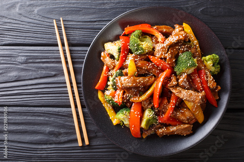 delicious Asian teriyaki beef with red and yellow bell peppers, broccoli and sesame seeds close-up on a plate. horizontal top view